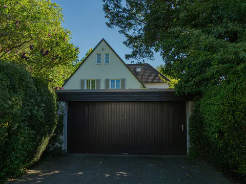 Een huis met een puntdak en een donkere garagepoort, tussen hagen