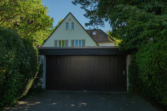 Een huis met een puntdak en een donkere garagepoort, tussen hagen