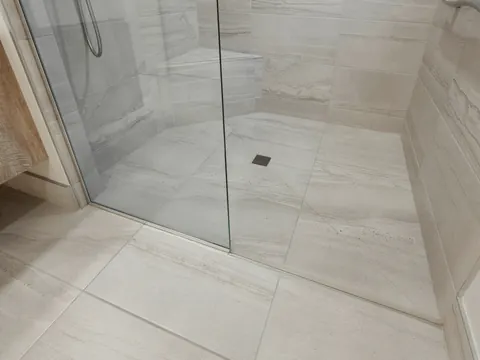 De vloer van een inloopdouche met een afvoerputje en een glazen wand