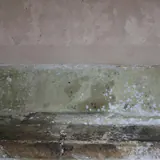 Vochtplekken en schimmel in een band onderaan een muur
