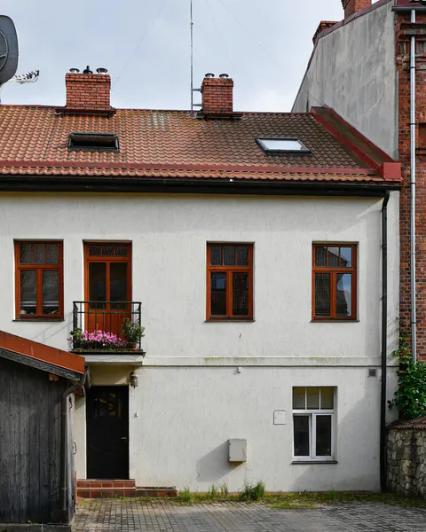 Een wit huis met rode dakpannen tussen bakstenen gebouwen