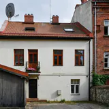 Een wit huis met rode dakpannen tussen bakstenen gebouwen