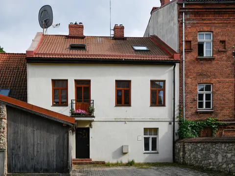 Een wit huis met rode dakpannen tussen bakstenen gebouwen