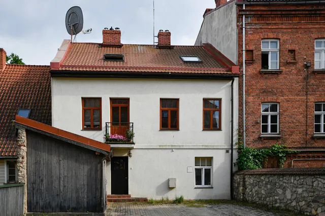 Een wit huis met rode dakpannen tussen bakstenen gebouwen