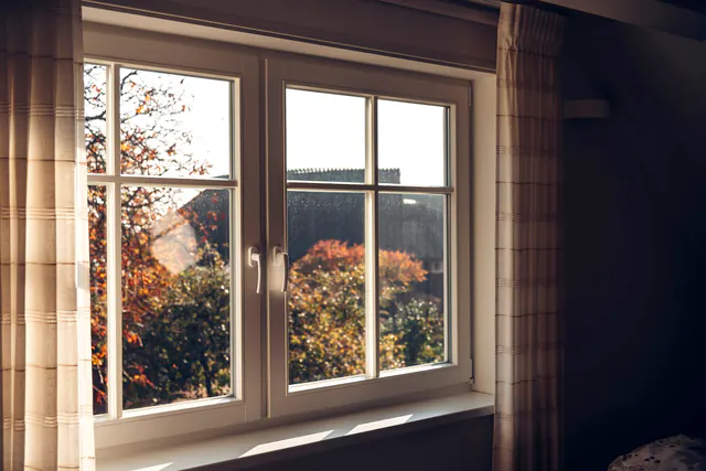 Een wit houten raam met twee vleugels, met herfstbomen erachter