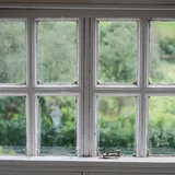 Een oud wit raam met kleine ruitjes, met een tuin erachter