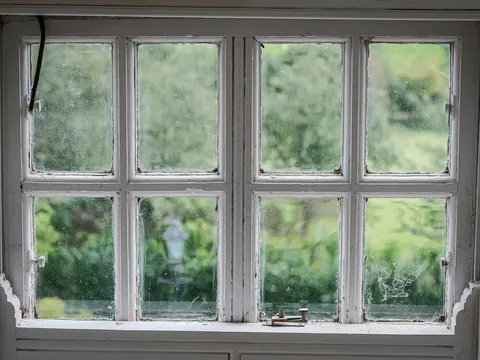 Een oud wit raam met kleine ruitjes, met een tuin erachter