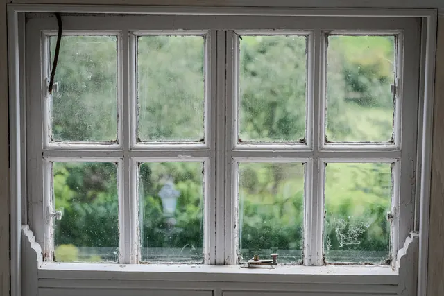 Een oud wit raam met kleine ruitjes, met een tuin erachter