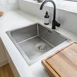 Een inox gootsteen met een afvoerputje, onder een raam