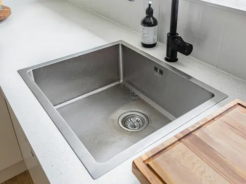 Een inox gootsteen met een afvoerputje, onder een raam