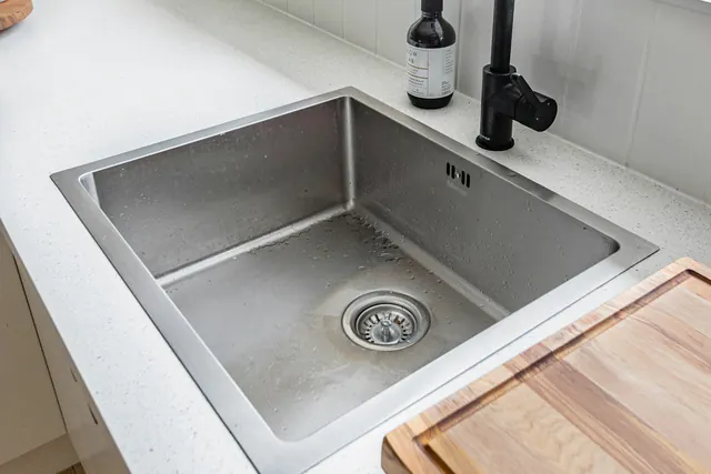 Een inox gootsteen met een afvoerputje, onder een raam