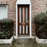 Een houten voordeur onder een boog in een bakstenen gevel