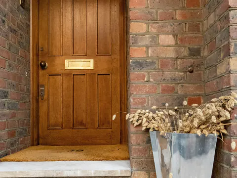 Een houten voordeur in een bakstenen portiek, met een plantenbak