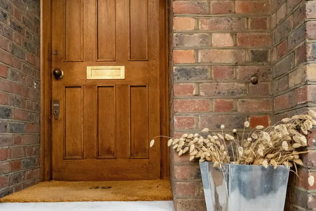 Een houten voordeur in een bakstenen portiek, met een plantenbak